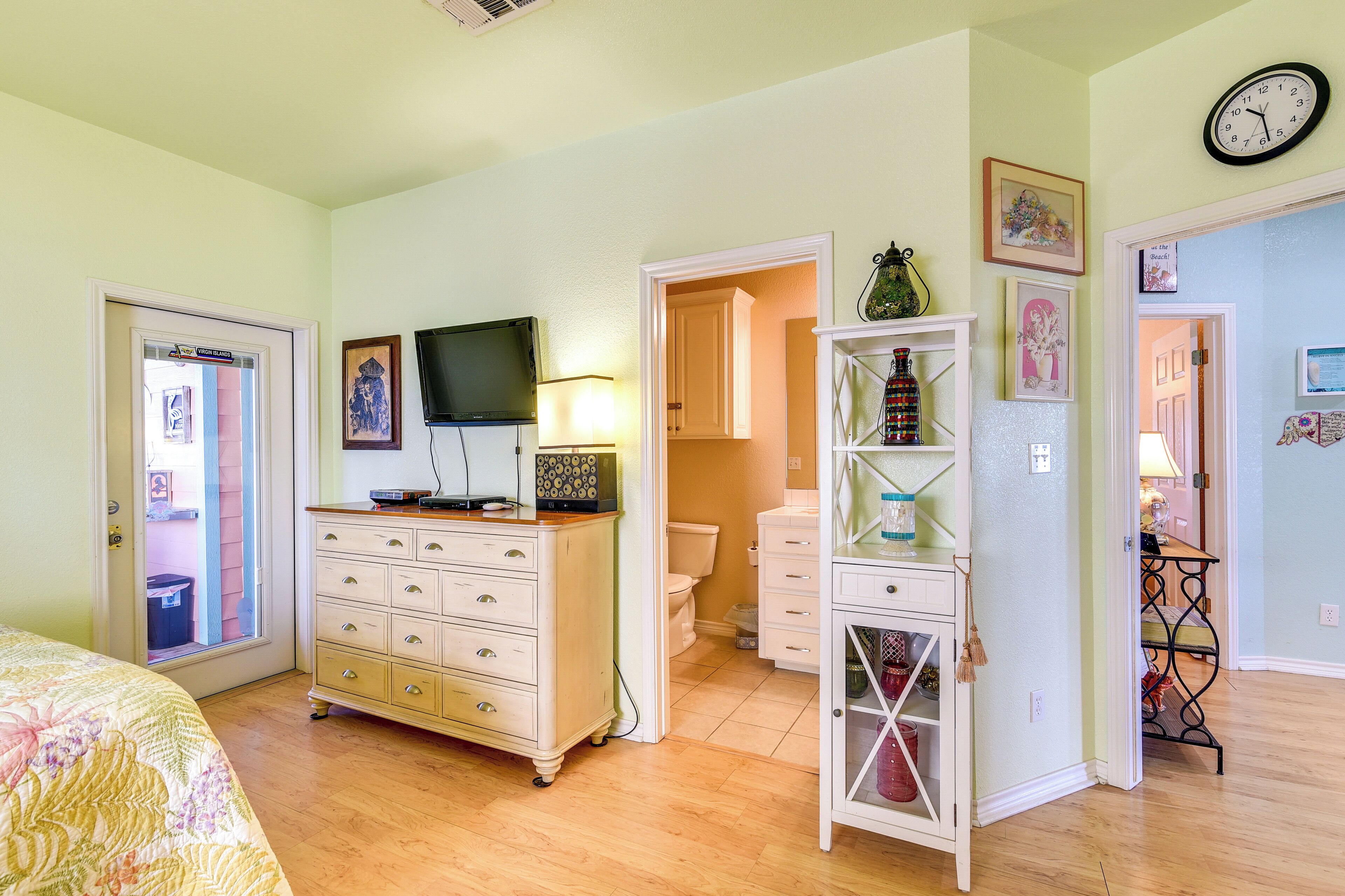 A bedroom with a bed, dresser, television, and a bathroom with a toilet and sink.
