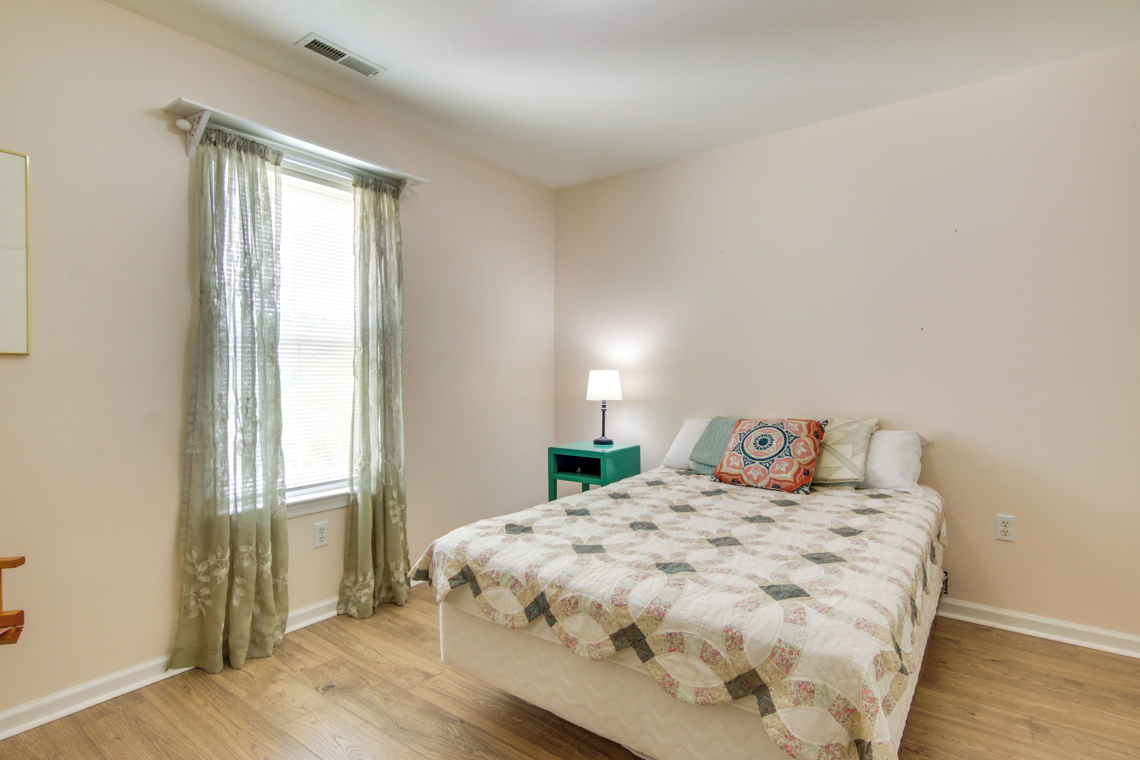 Un dormitorio con cama, mesita de noche, lámpara y ventana con cortinas.