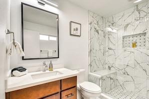 A modern bathroom with a white sink, a mirror, a toilet, and a shower area with marble walls. - Modern Home w/ Spacious Yard in Beaverton! (Beaverton)