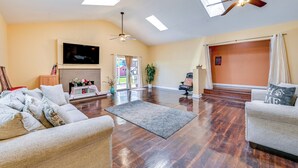 Un salon spacieux doté d’un plancher en bois franc, d’un ventilateur de plafond, d’un téléviseur à écran plat et d’une grande fenêtre.