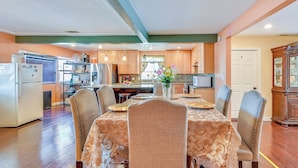 Une cuisine spacieuse équipée d’appareils électroménagers modernes, un coin repas avec une table dressée pour quatre personnes et un grand meuble en bois.