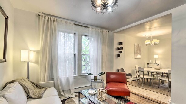 A modern living room with a glass coffee table, a red leather chair, a white sofa, and a dining area with a table and chairs.
