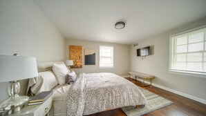 A bedroom with a bed, bedside table, lamp, artwork, window, and a television on the wall. - Vacation Rental Near Cleveland, Ohio: 6 Mi Away! (University Heights)