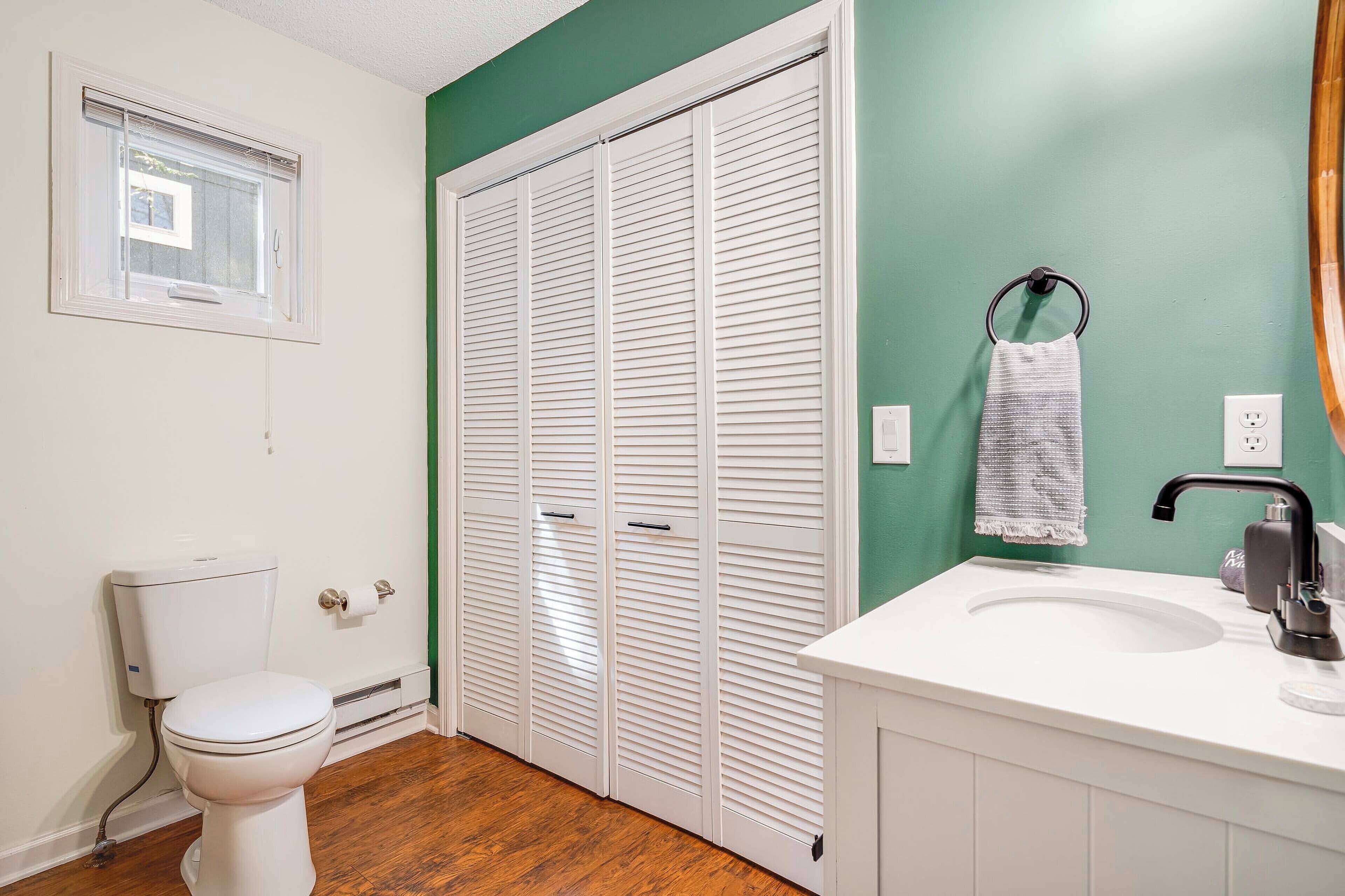 A bathroom with a toilet, a white sink, a mirror, and a green wall.