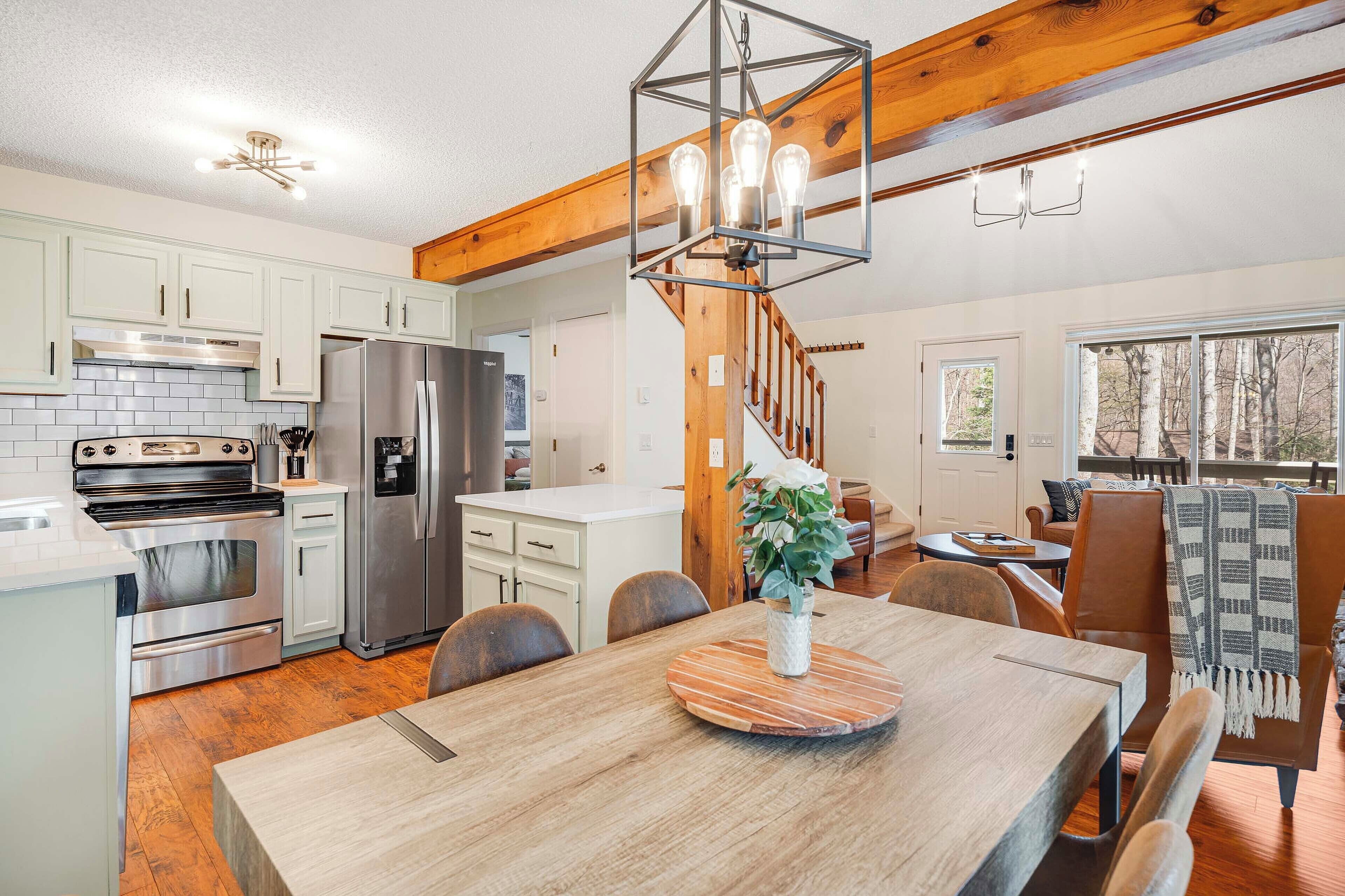A modern kitchen with stainless steel appliances, a dining area with a wooden table, and a staircase leading to a loft bedroom.