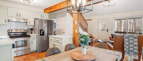 A modern kitchen with stainless steel appliances, a dining area with a wooden table, and a staircase leading to a loft bedroom.