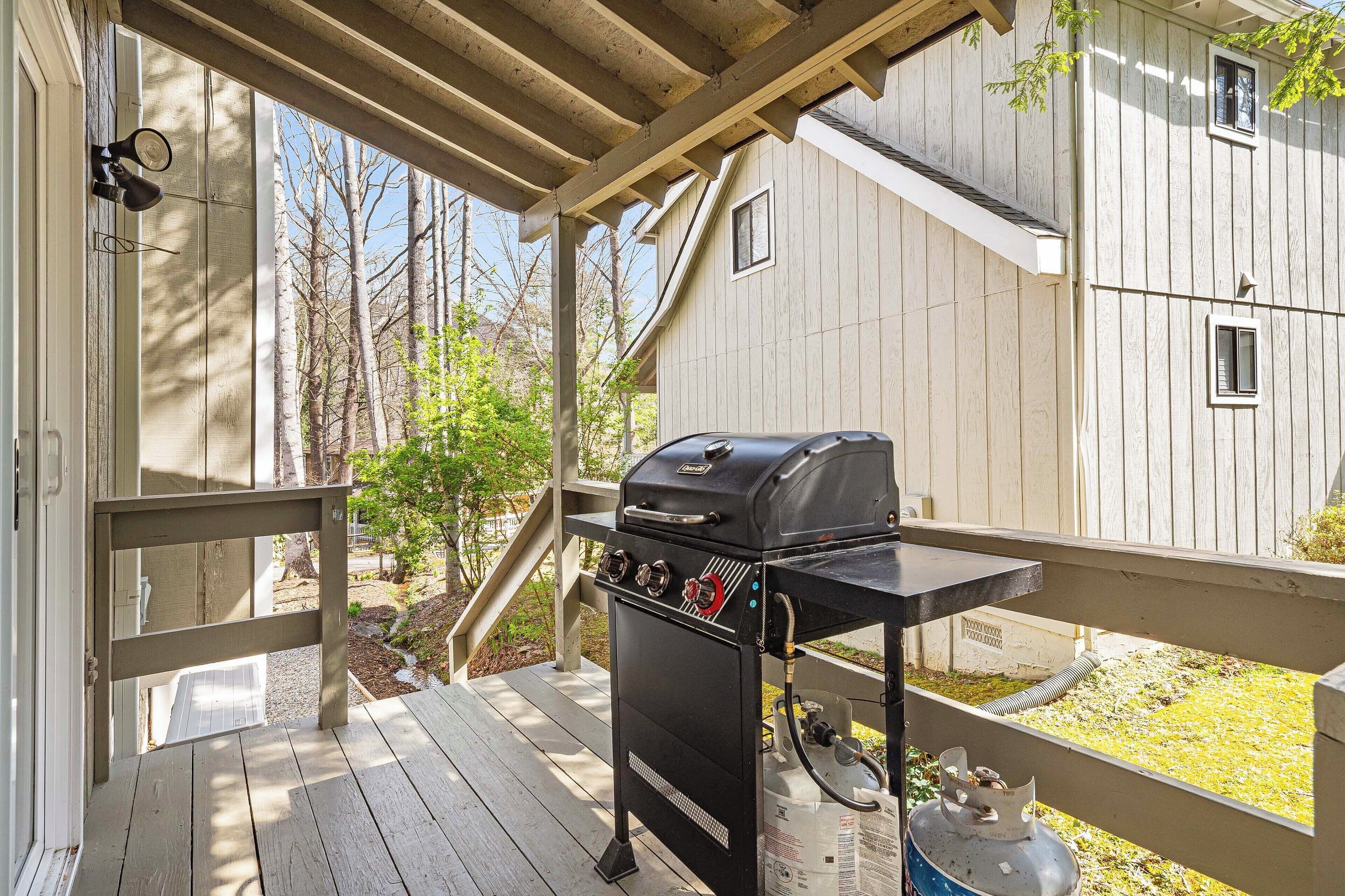 A covered outdoor area with a barbecue grill, wooden deck, and a view of a house with a white exterior.