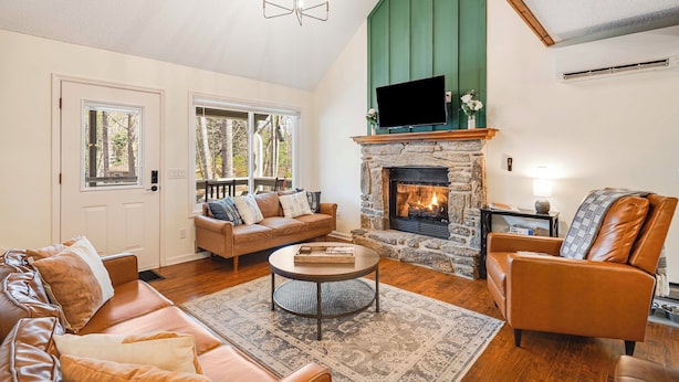A cozy living room with a stone fireplace, leather sofas, and a large window overlooking a deck.