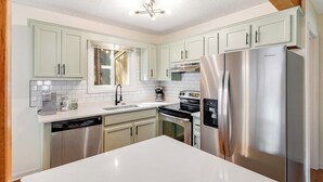 A modern kitchen with light green cabinets, stainless steel appliances, and a white countertop.