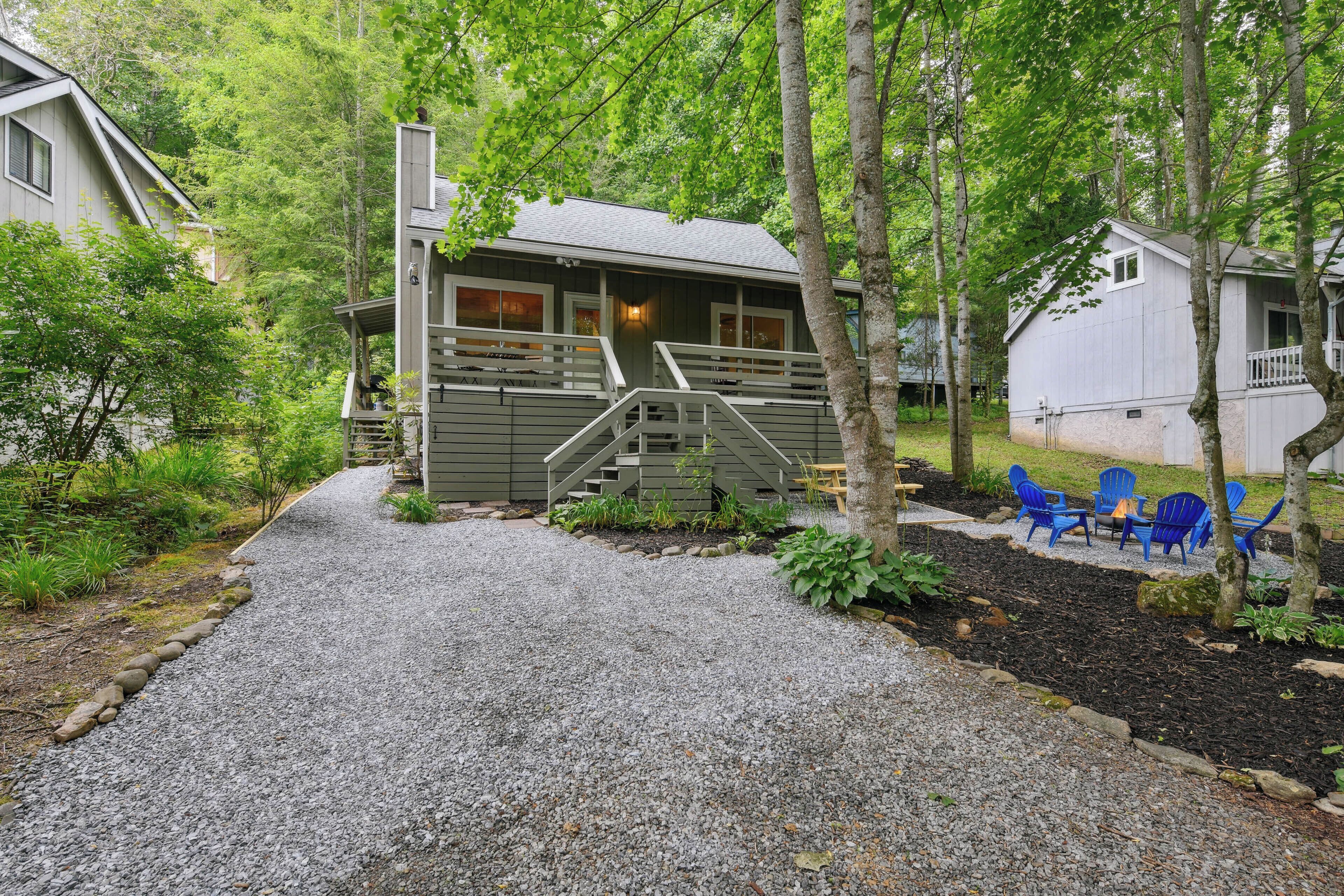 A cabin with a gravel driveway, a wooden staircase, and a deck with blue chairs.