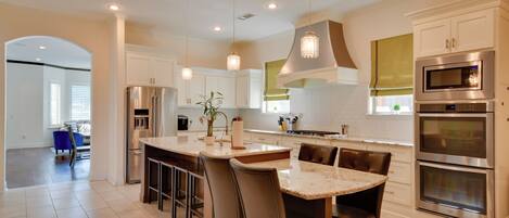 A modern kitchen with a central island, bar stools, stainless steel appliances, and pendant lighting.
