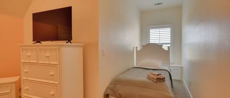 A bedroom with a bed, a dresser, a television on top of the dresser, and a window with blinds.