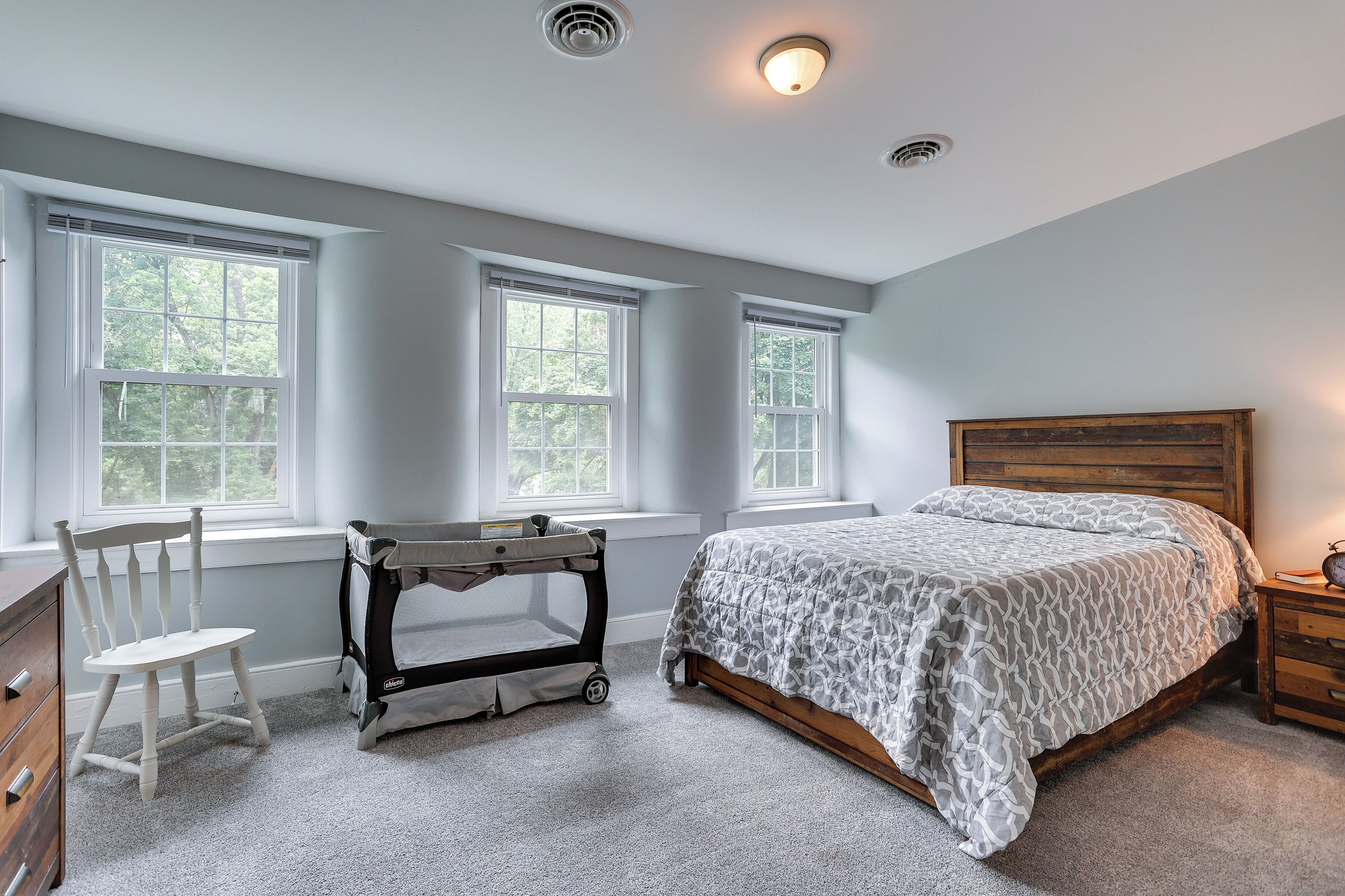 A bedroom with a bed, a crib, a chair, and a dresser.