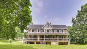 A large stone house with a wrap-around porch, multiple windows, and a well-maintained lawn. - Large Historic Home in Pennsylvania Dutch Country! (Coatesville)