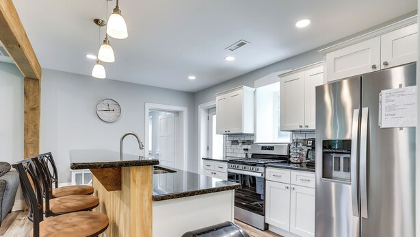 A modern kitchen with white cabinets, stainless steel appliances, a wooden island with bar stools, and a clock on the wall. - Large Historic Home in Pennsylvania Dutch Country! (Coatesville)