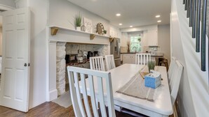 A dining area with a white table and chairs, a fireplace, and a kitchen in the background. - Large Historic Home in Pennsylvania Dutch Country! (Coatesville)
