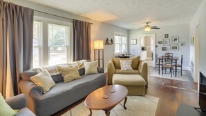 A living room with a sofa, ottoman, and coffee table, a dining area with a table and chairs, and a ceiling fan.