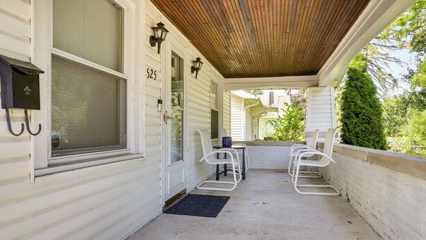 A covered porch with a concrete floor, white metal chairs, a small table, and a mailbox.