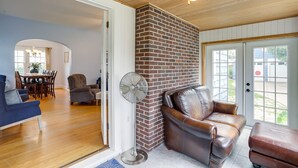Una sala de estar con chimenea de ladrillo, sofá de cuero y un ventilador de pie.