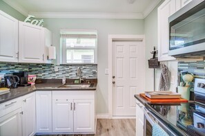A modern kitchen with white cabinets, a tiled backsplash, a window with blinds, a microwave, and a stove. - Cozy Melbourne Hideaway Near Beaches, Downtown! (Melbourne)