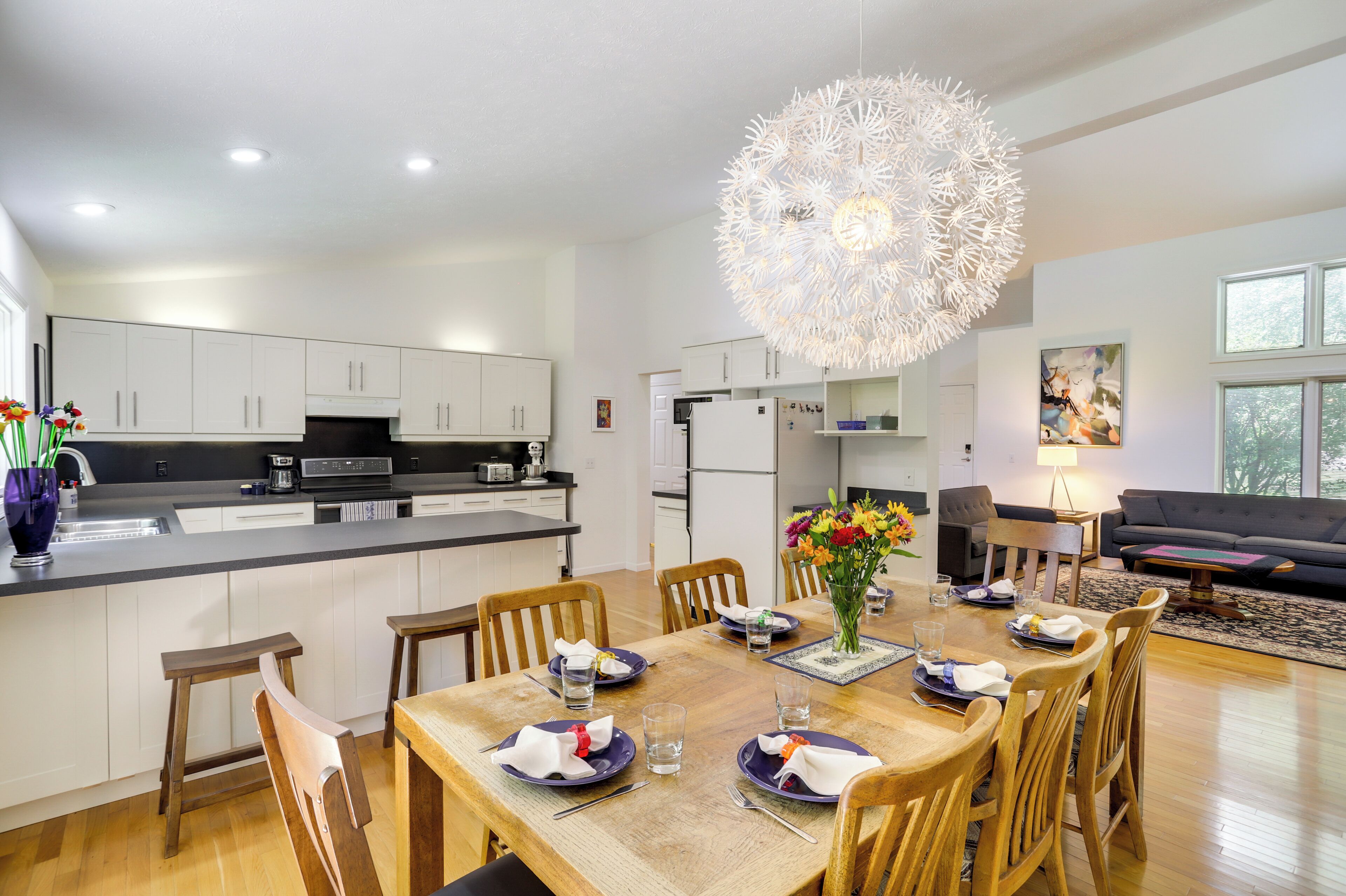 A modern kitchen with white cabinets, a central island, and a dining area with wooden chairs and a table set for four.