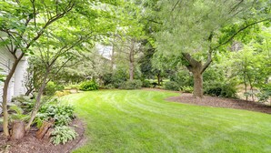 A well-maintained garden with a variety of trees and shrubs, a neatly trimmed lawn, and a wooden deck. - Granger Gathering Place, 4 Mi to Notre Dame (Granger)