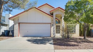 Une maison à deux étages avec un garage, une façade en pierre et un arbre dans le jardin.