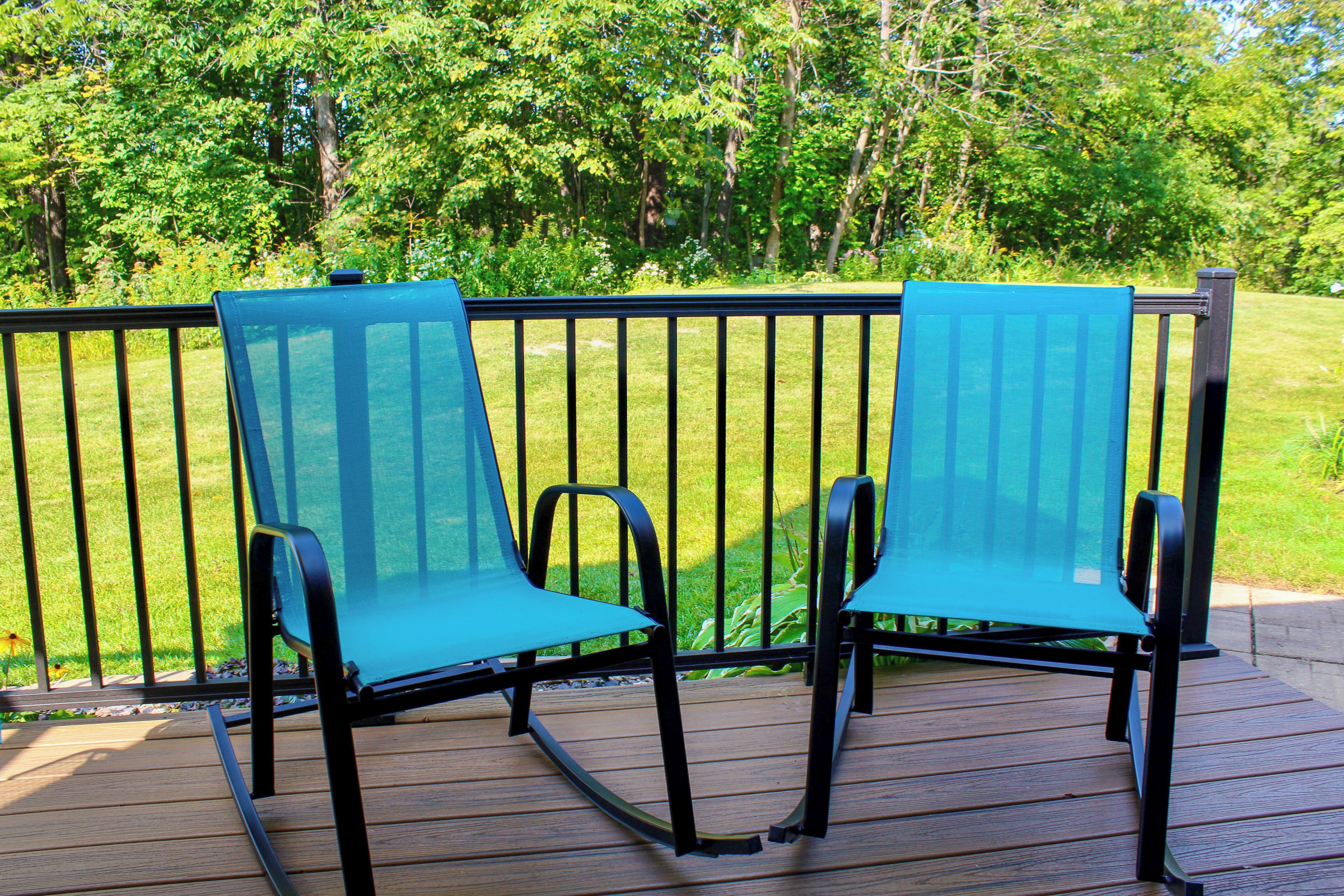Two blue chairs on a wooden deck with a metal railing, surrounded by greenery.