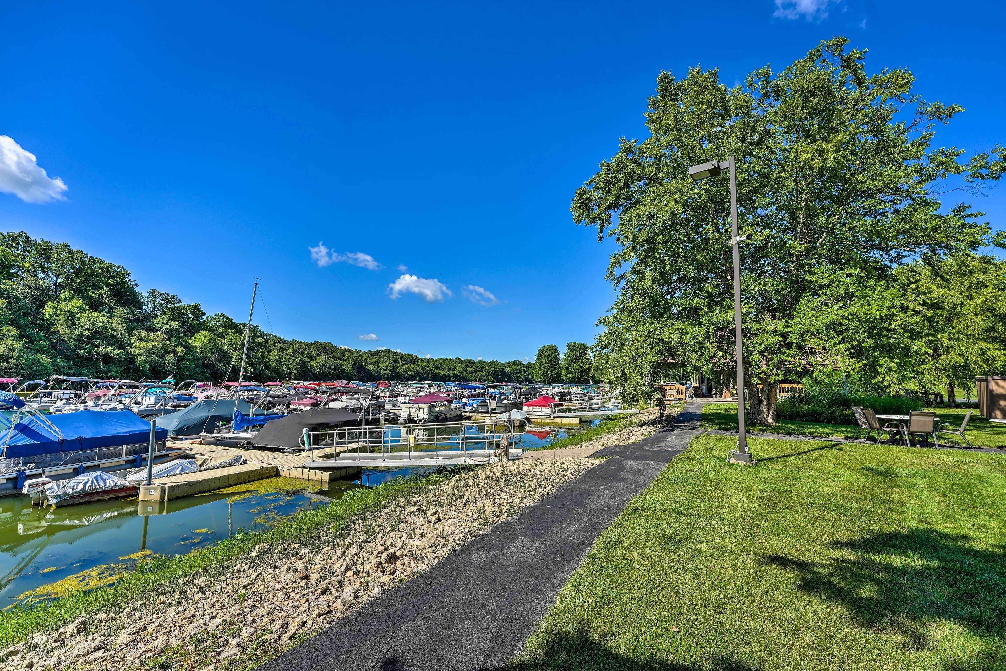 A marina with boats docked, a walking path, and a grassy area with trees.