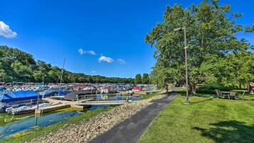 A marina with boats docked, a walking path, and a grassy area with trees.