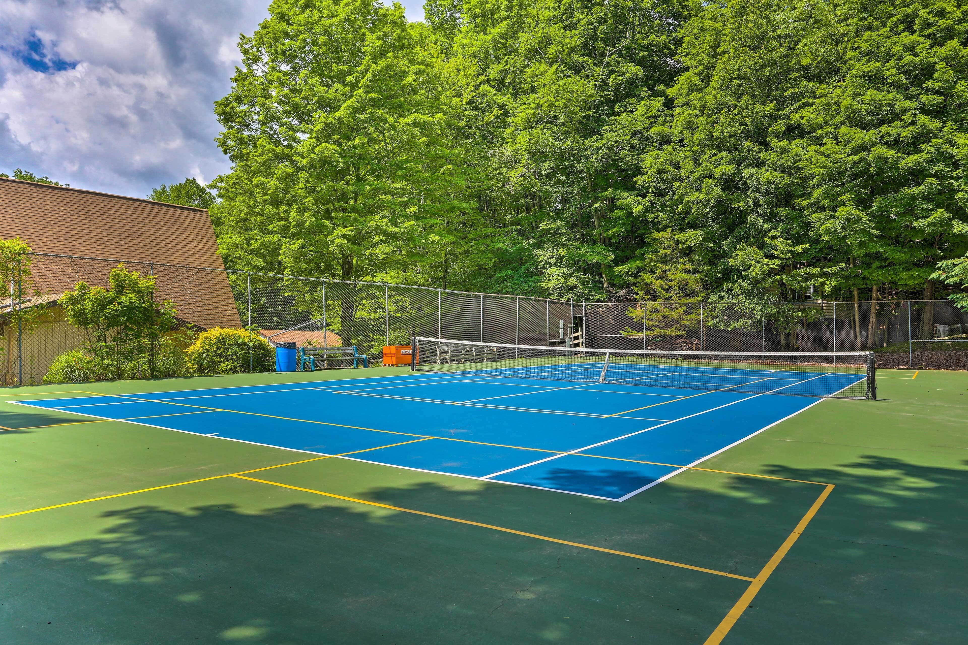 Un court de tennis avec un filet, entouré d’arbres et d’une clôture.