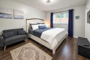 A bedroom with a bed, a grey sofa, a small bench, a rug, and a window with curtains. - Centrally Located Reno Retreat w/ Patio & Yard (Reno)