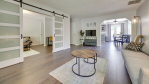 Un grand salon comprenant un canapé, une table basse et un téléviseur. Une porte coulissante donne accès à une autre pièce.