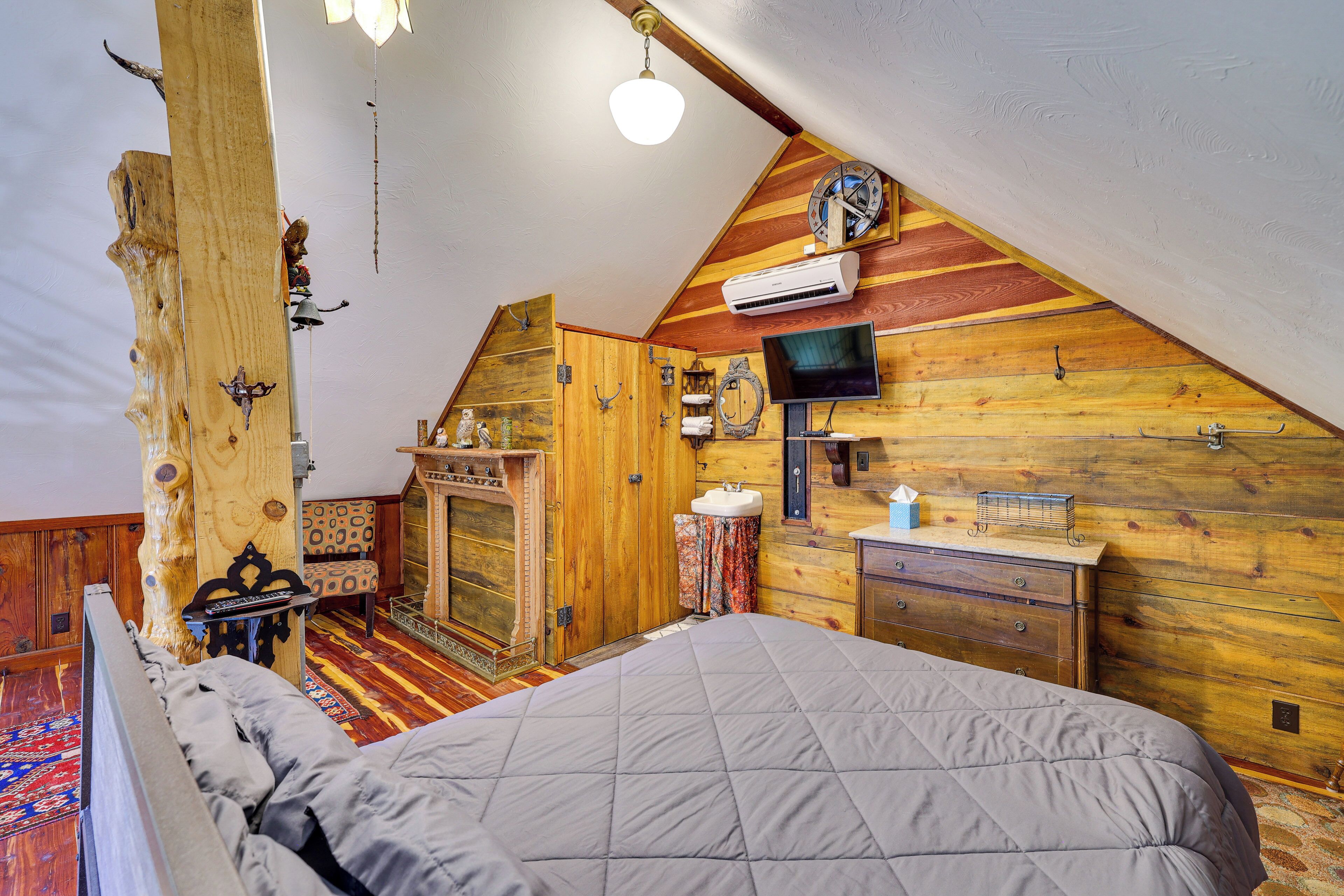 Un dormitorio acogedor en el ático con una cama, paredes de madera, chimenea y televisor.