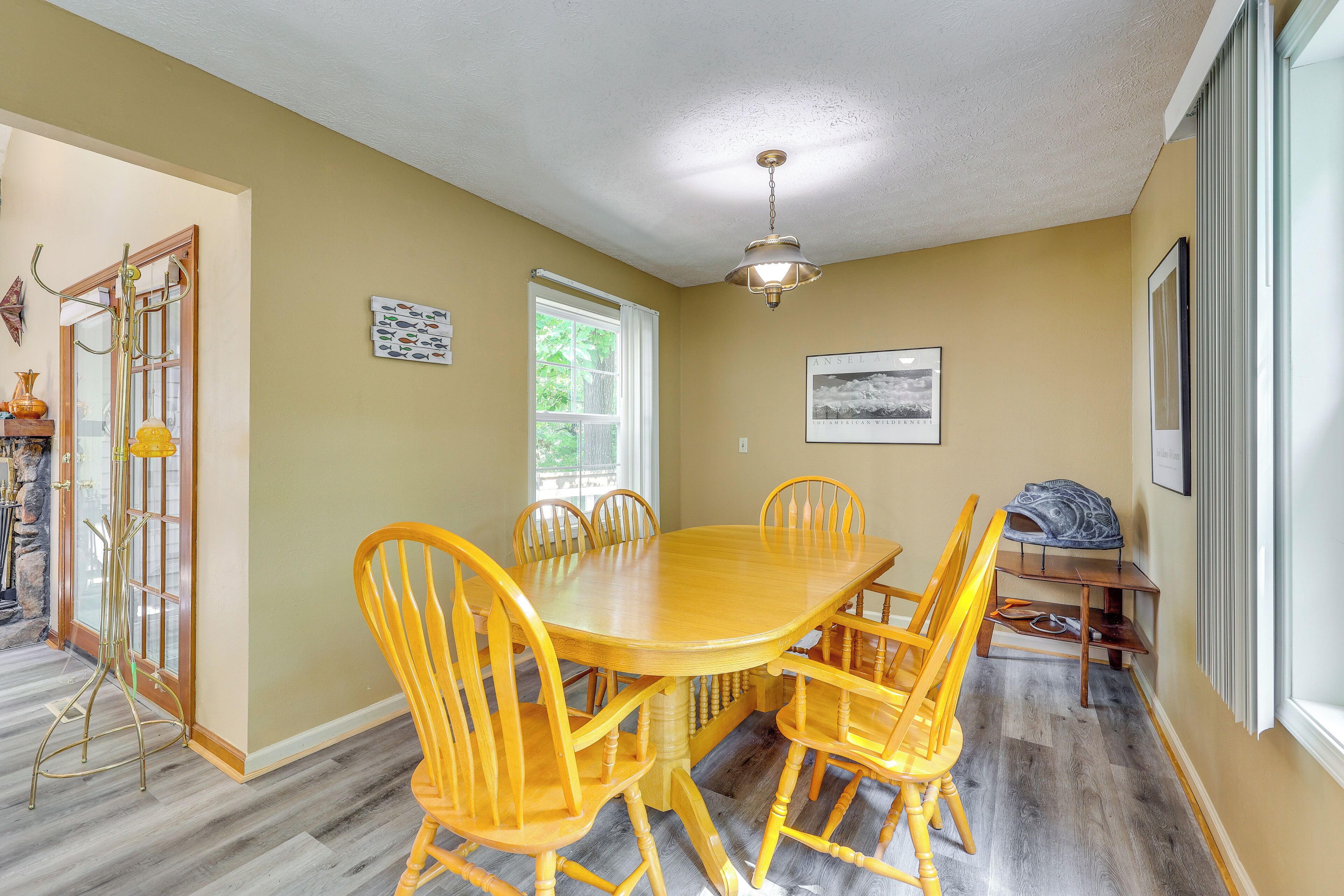 A dining area with a wooden table and chairs, a ceiling fan, and a window with a view of greenery.