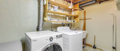 Uma lavanderia com duas máquinas de lavar Whirlpool, prateleiras de madeira acima e um esfregão no chão.