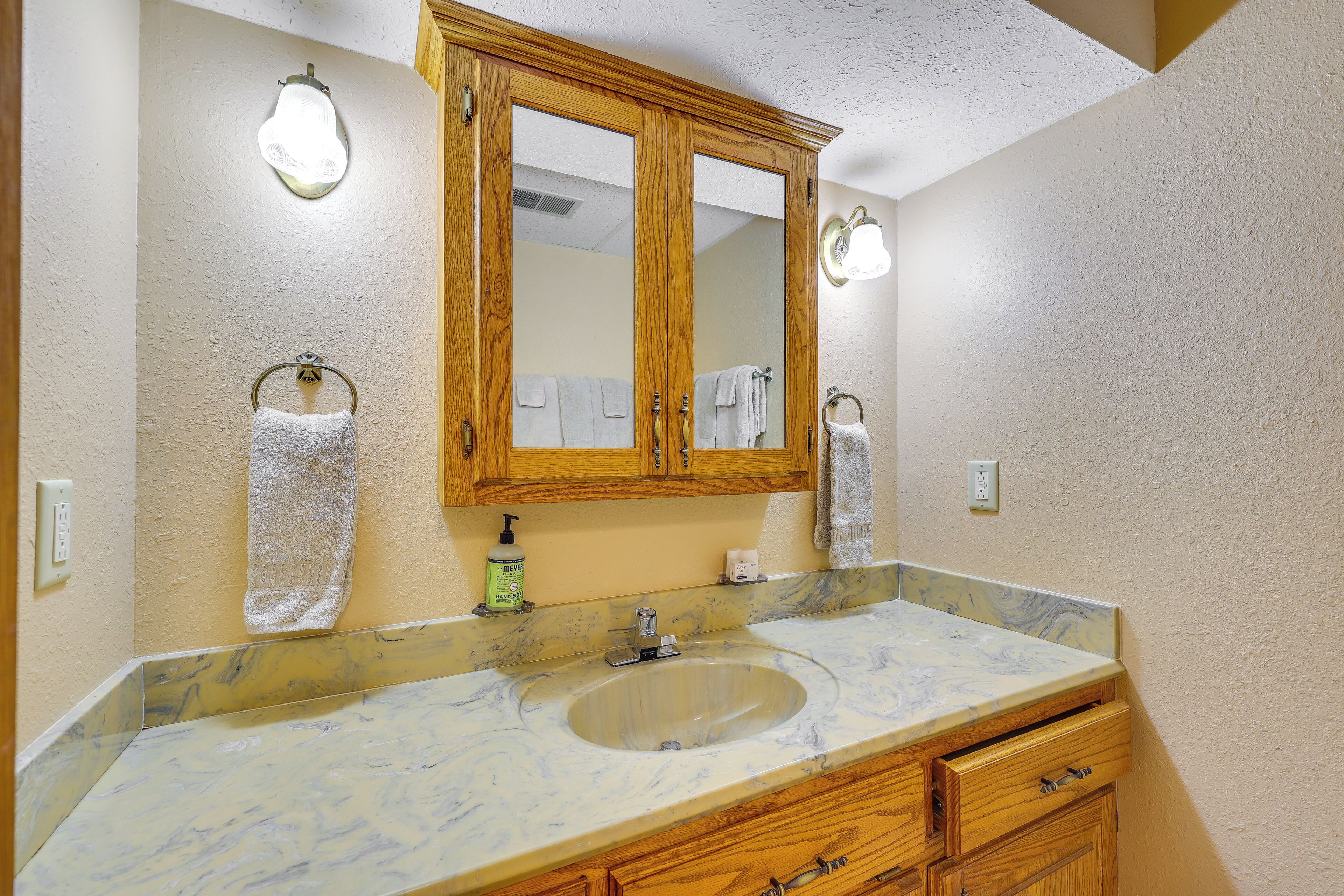 A bathroom with a marble sink, wooden cabinets, and a large mirror.