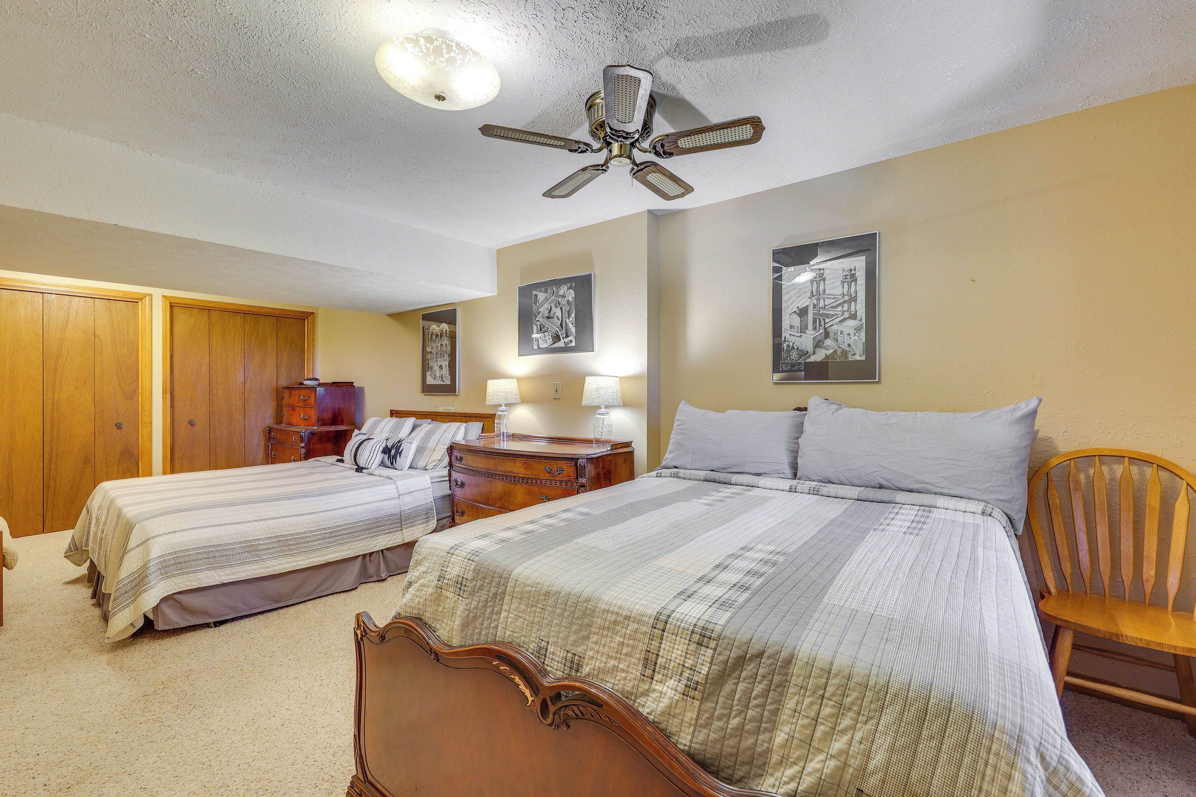 A bedroom with two single beds, a wooden wardrobe, a nightstand with a lamp, and a ceiling fan.