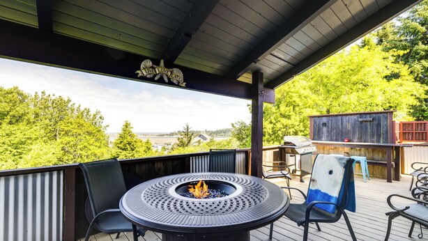 Een overdekt terras met een ronde tafel en stoelen, een vuurkuil en een barbecueplaats.