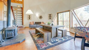 Amplia sala de estar con escalera de madera, un sofá, una mesa de centro y una mesa de futbolín.
