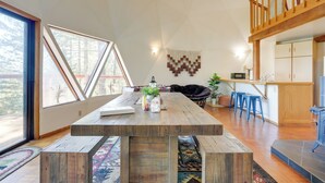 Amplia sala de estar con una gran mesa de madera, un sofá negro y una cocina con armarios de madera y taburetes de bar azules.