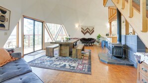 Amplia sala de estar con un ventanal grande, una escalera de madera y una chimenea de piedra.