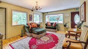 A cozy living room with a red and white patterned rug, two green upholstered sofas with red and gold cushions, a wooden coffee table, and a chandelier. - Eureka Springs Rental - Walk to Downtown! (Eureka Springs)