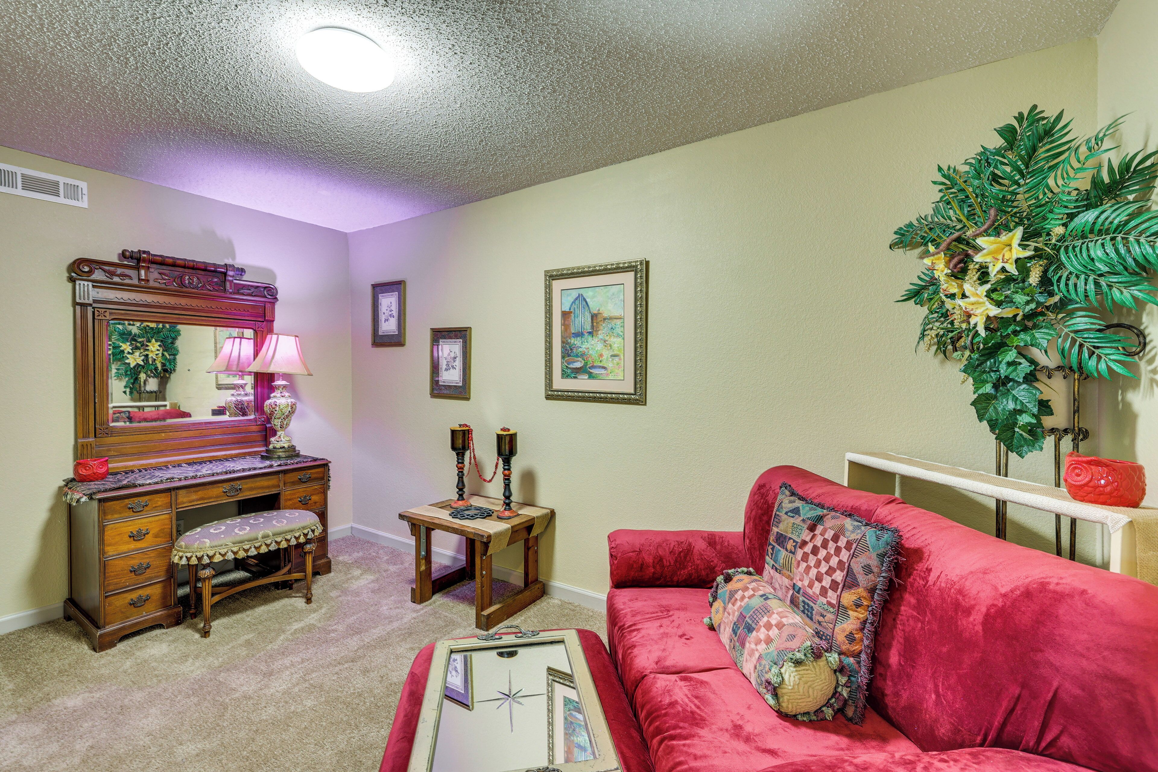 A living room with a red sofa, a wooden dresser, a mirror, and a potted plant.