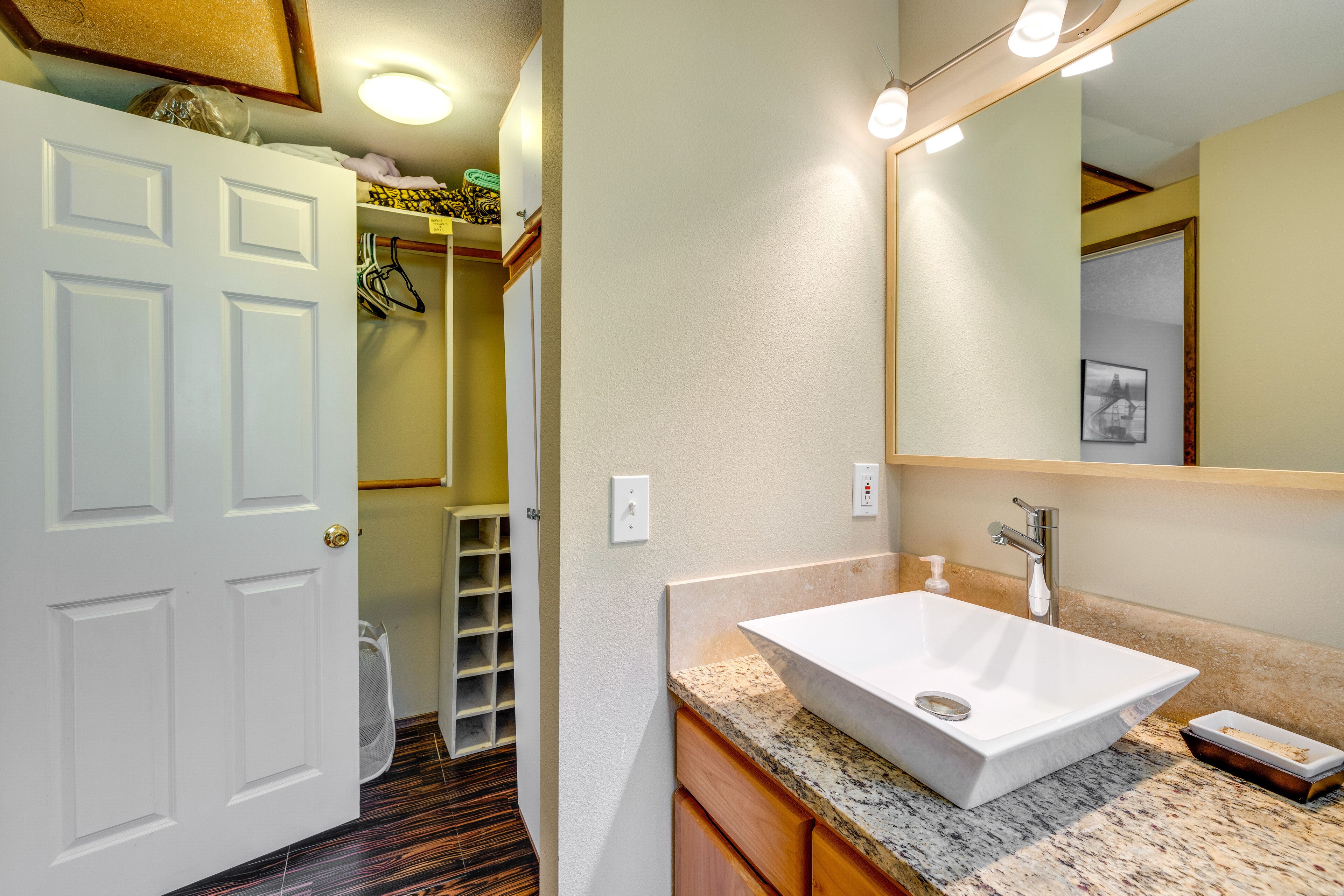 A bathroom with a white sink, wooden cabinets, a large mirror, and a door leading to a hallway.