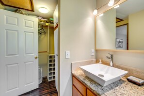Un baño con lavamanos blanco, armarios de madera, un espejo grande y una puerta que da a un pasillo.