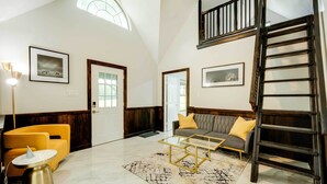 A spacious living room with a high ceiling, a staircase, and a large window.