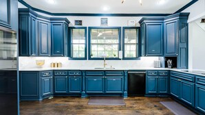 A modern kitchen with dark blue cabinetry, a white countertop, and a wooden floor.