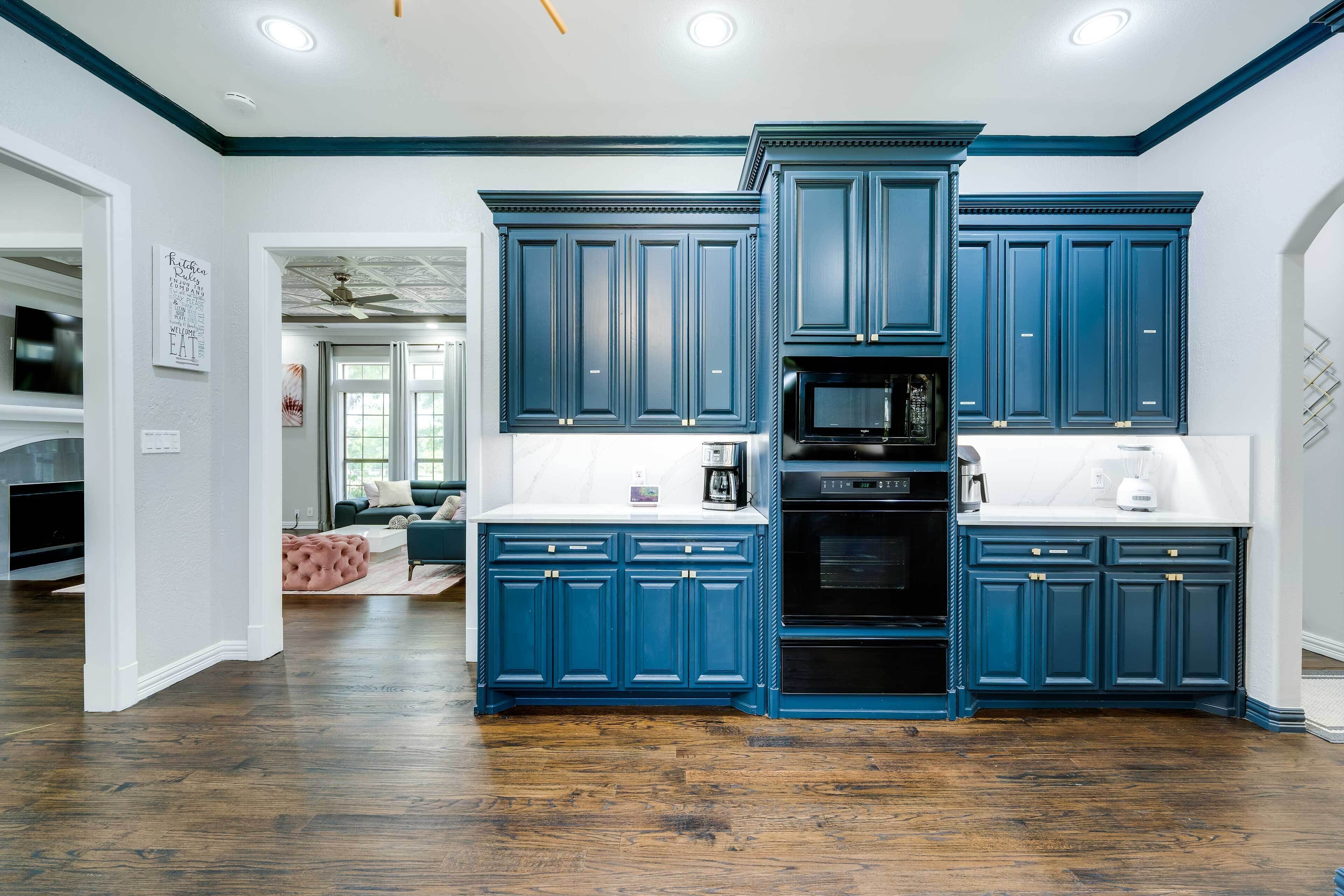 Ett kök med mörkblå skåp, en svart mikrovågsugn och en vit bänkskiva.