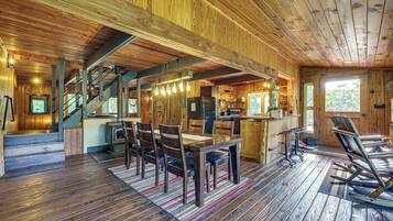 A wooden cabin interior with a dining area, kitchen, and a staircase.